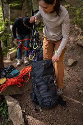Eine Frau räumt unterschiedliche Karabiner in den Rucksack Alpinisto 30.