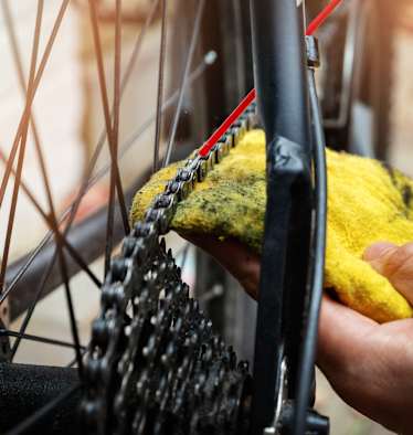 Hand die mit rotem Schlauch und gelbem Lappen eine Fahrradkette schmiert