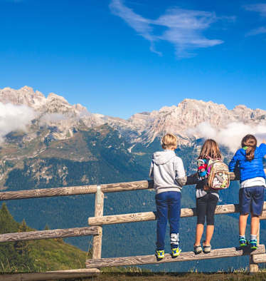 Drei Kinder stehen auf einem Holzzaun und blicken in die Berge.