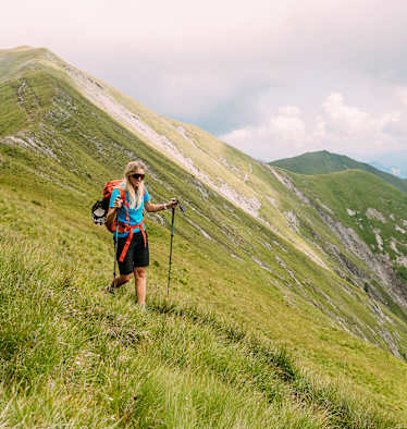 Wanderin geht mit Wanderstöcken über begrasten Berg