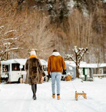 Ein Pärchen geht mit einem Rodel über einen Campingplatz im Winter.