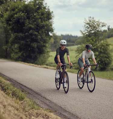 Zwei Radfahrer fahren auf einer ruhigen Landstraße im Mühlviertel bei der Bike Experience, umgeben von grüner Natur und sanften Hügeln.