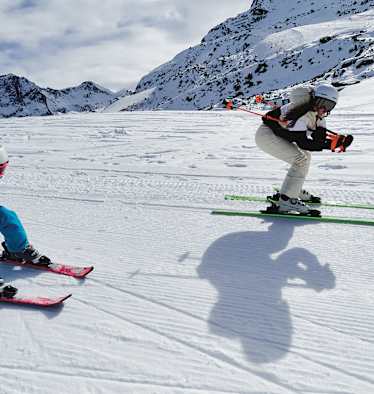 Eine Frau und ein Mädchen fahren gemeinsam Ski und nehmen dabei die Schussposition ein.