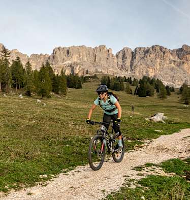 Eine Frau fährt auf einem Mountainbike. Hinter ihr liegt ein Dolomitenpanorama.