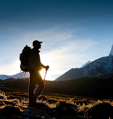 Ein Wanderer im Gegenlicht. Im Hintergrund ein schneebedeckter Berg.
