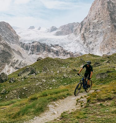 Mann fährt vor eindrucksvoller Bergkulisse mit dem Mountainbike bergab