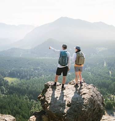 Zwei Personen im Wanderoutfit stehen auf einem Felsen und genießen die Aussicht.