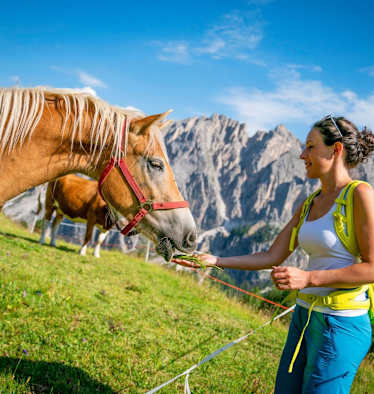 Eine Frau füttert ein Pferd auf der Alm
