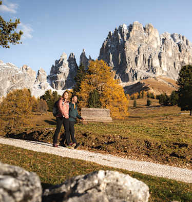 Zwei Wanderer marschieren auf einem Schotterweg durch die bunte Herbstlandschaft der Seiser Alm.