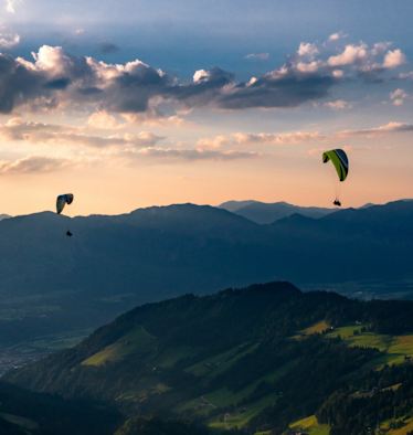 Zwei Personen paragleiten über ein Tal in der Wildschönau.