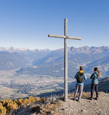 Panorama in Bruneck in Südtirol mit 2 Wanderern und einem Holzkreuz