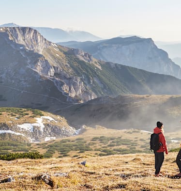 Zwei Wanderer stehen im Herbst auf dem Raxplateau und blicken in die Ferne