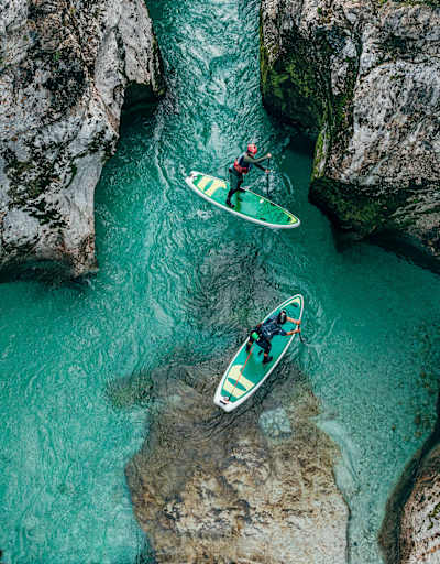 Zwei Stand-up-Paddler treiben in einem türkisblauen Fluss, der Soča