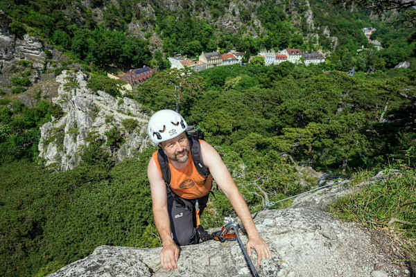 Mann klettert im Mödlinger Klettersteig über einen Felsen; im Hintergrund: grüner Wald