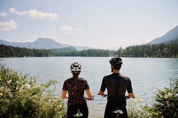 Zwei Radfahrer stehen am Ufer des Hintersees bei Ramsau im Berchtesgaden und blicken über den See.