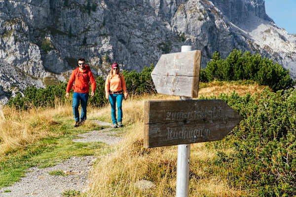 Zwei Wanderer auf der Karnischen Milchstraße und ein Wanderschild aus Holz im Vordergrund.