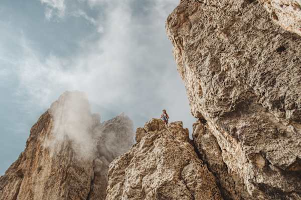 Klettersteig Dolomiten, Eggental: Kletterin steht auf einer der Felszinnen, während leichter Nebel von links hereinzieht.