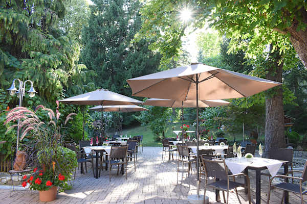 Der ruhige Gastgarten des Kloepferkellers in Eibiswald: schon gedeckte Tische, Schirme und viel Grün