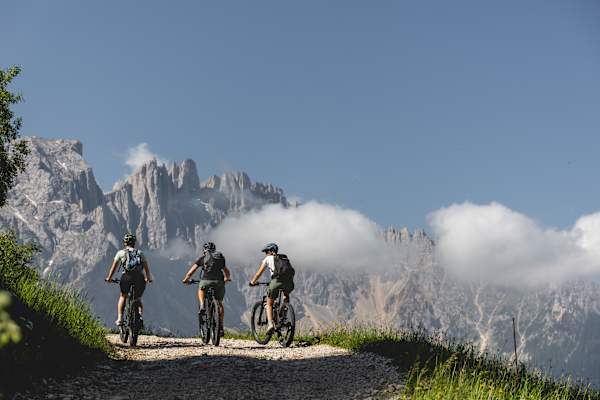 Drei Mountainbiker auf der Latemar Ronda im Eggental vor der Kulisse des Latemar Massivs.