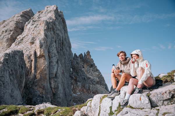 Zwei Wanderer sitzen auf einem Felsen vor einer Felszinne im Latemarmassiv, Eggental.