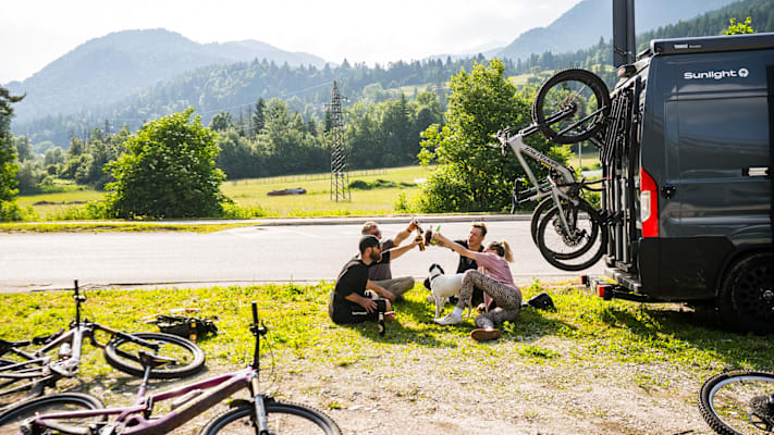 Eine Gruppe von Van Reisende mit dem Bike auf der Wiese sitzend und trinken Bier als Abkühlung nach einer Radtour.