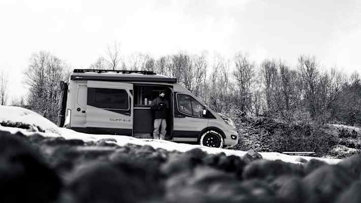 Ein Campervan steht in einer verschneiten Landschaft, umgeben von kahlen Bäumen, ideal für Abenteuer in Nord-Norwegen.