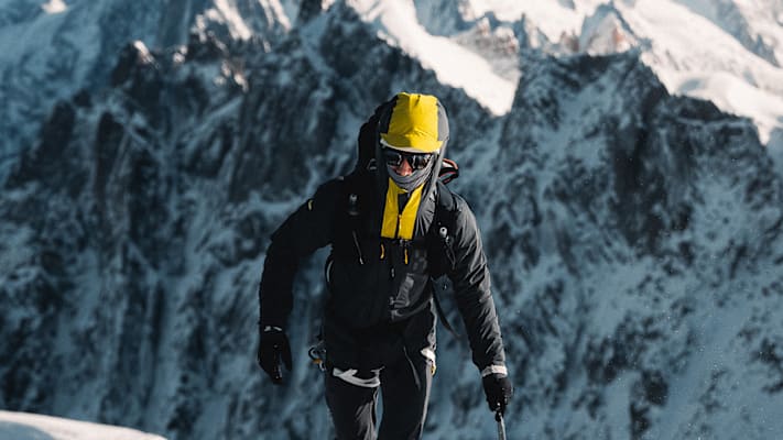 Ein Mann am Berg umgeben von Schnee und Natur trägt warme Winterkleidung.