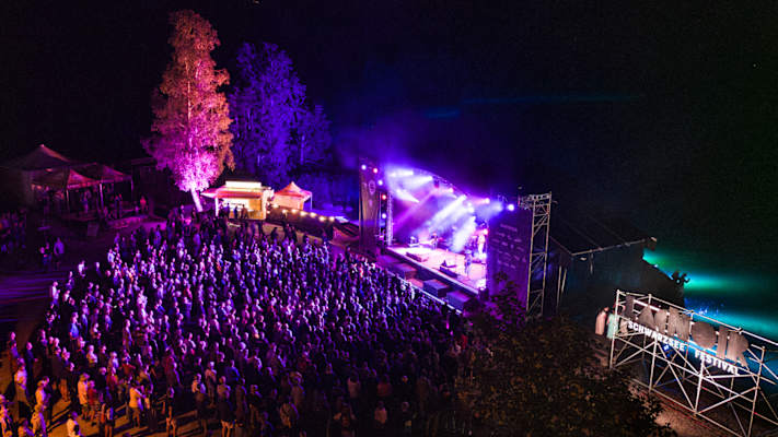 Eine Open Air-Bühne mit einer tanzenden Menschenmenge am Schwarzsee mit einer bunten Lichtershow.