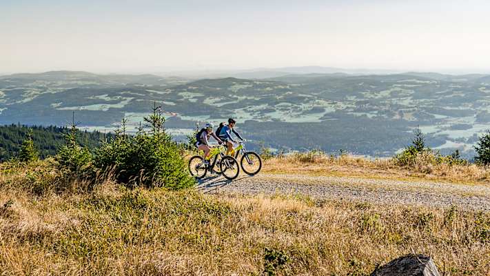 Zwei Mountainbiker auf einer Schotterstraße mit Panoramablick über die hügelige Landschaft des Mühlviertels, Oberösterreich.