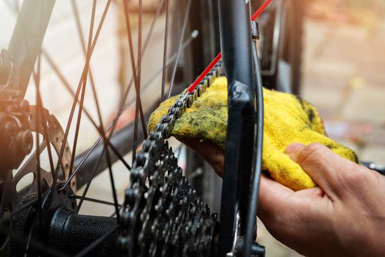 Hand die mit rotem Schlauch und gelbem Lappen eine Fahrradkette schmiert