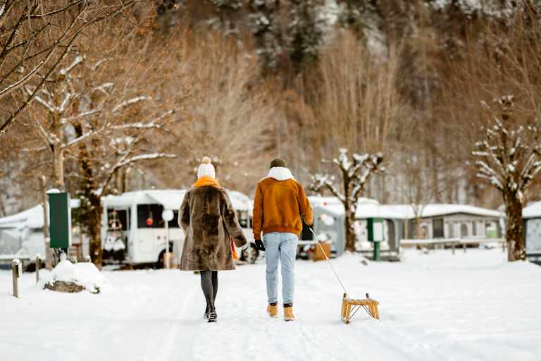 Ein Pärchen geht mit einem Rodel über einen Campingplatz im Winter.