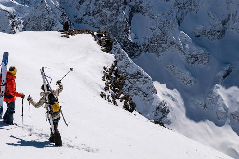 Auf einem schneebedeckten Hang stehen zwei Skitourengeher und zeigen in die Ferne. Sie sind mit der Bergtagen-Kollektion von Fjällräven ausgerüstet.