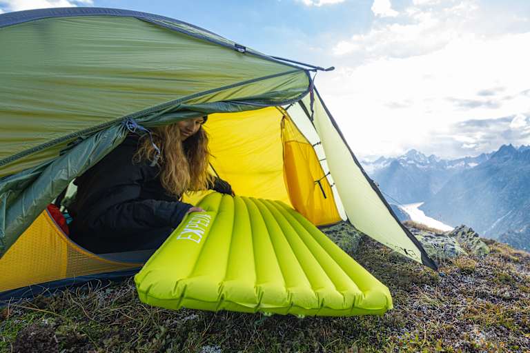 Eine Frau sitzt in einem Zelt und zieht eine Schlafmatte von Exped hinein.