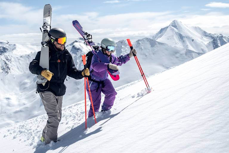 Ein Skifahrer und eine Skifahrerin gehen eine Piste in Ischgl hinauf.