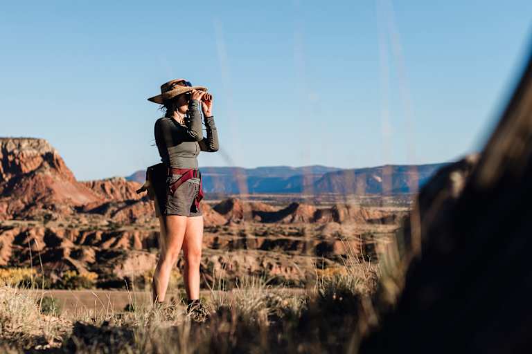 Eine Frau steht draußen in der Natur und blickt durch den CL Companion von Swarovski Optik.