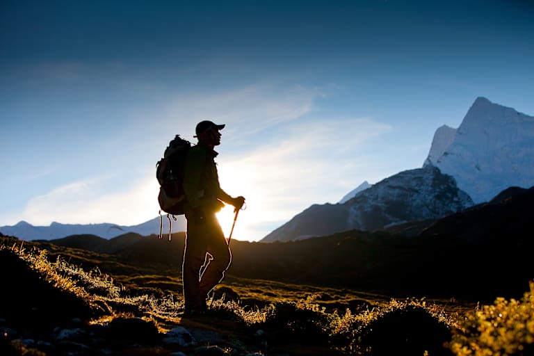 Ein Wanderer im Gegenlicht. Im Hintergrund ein schneebedeckter Berg.