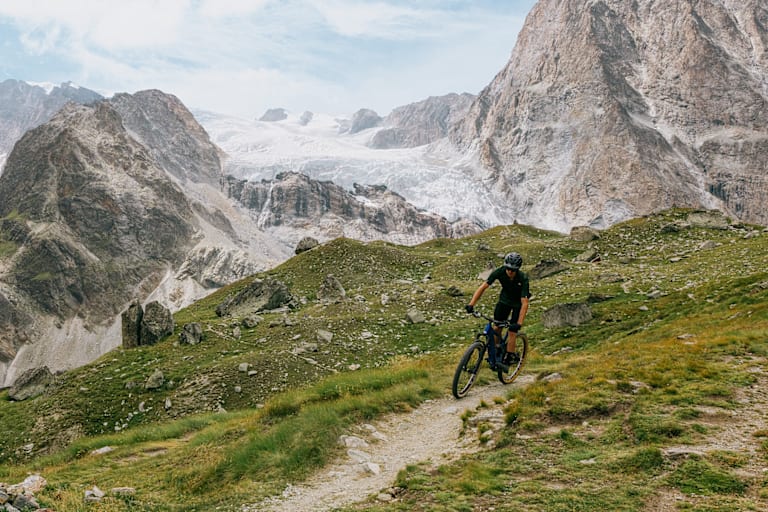 Mann fährt vor eindrucksvoller Bergkulisse mit dem Mountainbike bergab