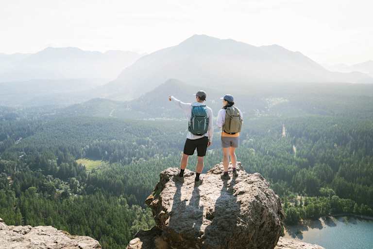 Zwei Personen im Wanderoutfit stehen auf einem Felsen und genießen die Aussicht.