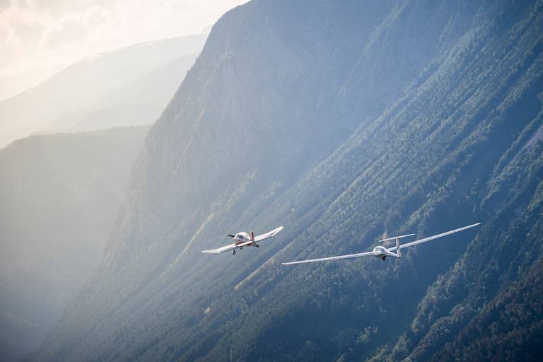 Zwei Flugzeuge vor nebelverschleierten Bergen.