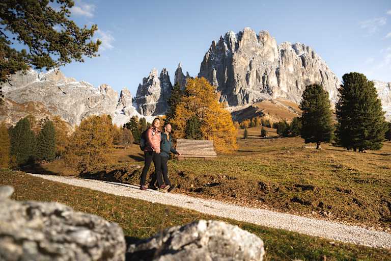 Zwei Wanderer marschieren auf einem Schotterweg durch die bunte Herbstlandschaft der Seiser Alm.