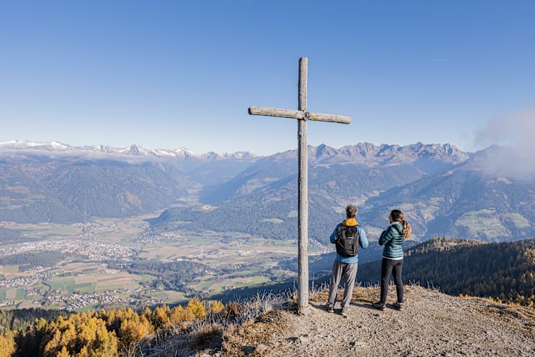 Panorama in Bruneck in Südtirol mit 2 Wanderern und einem Holzkreuz