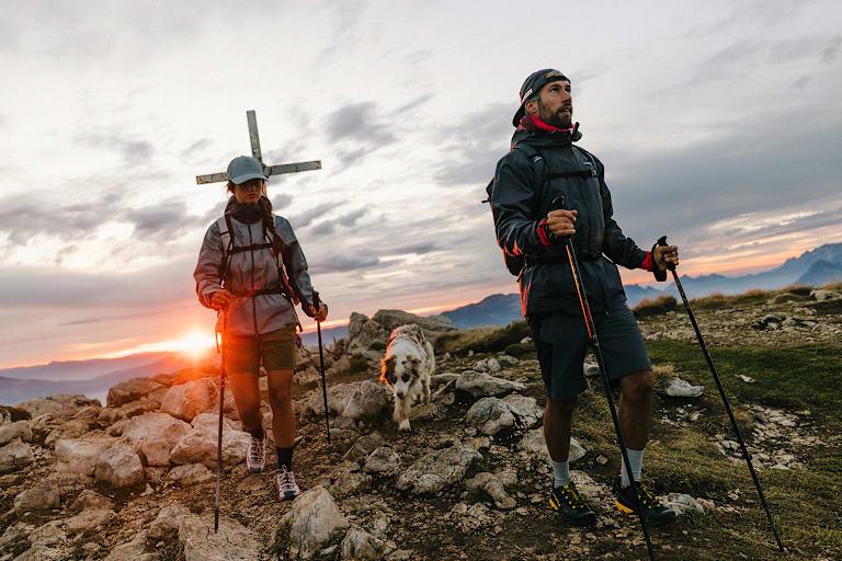 Ein Paar mit Hund wandert am Berg bekleidet mit Klediung von La Sportiva.