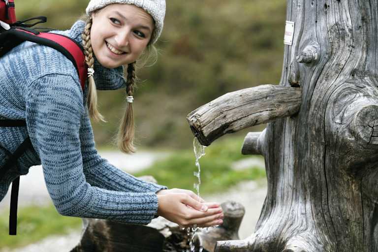 Wanderin schöpft Wasser aus einem Brunnen