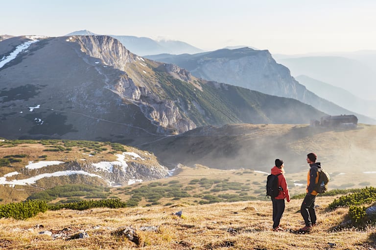 Zwei Wanderer stehen im Herbst auf dem Raxplateau und blicken in die Ferne