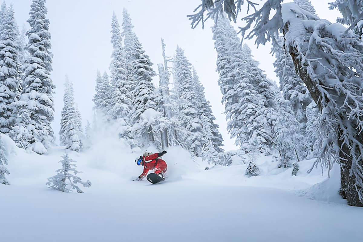 Eine Person fährt Snowboard im Wald im Winter in roter Ausrüstung.