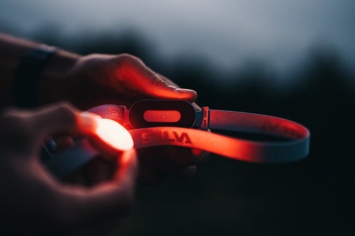 Eine orange leuchtende Stirnlampe von Silva wird von einer Person in der Hand gehalten.