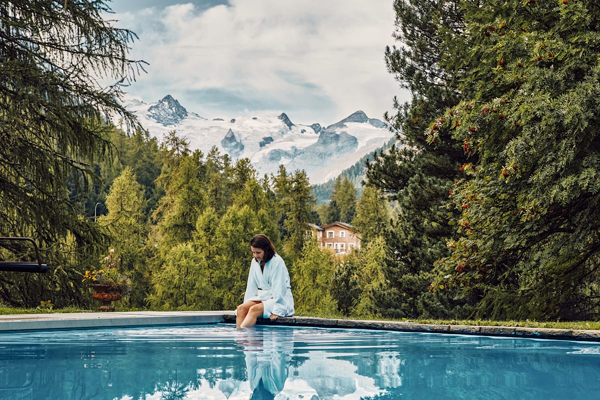 Eine Frau am Pool umgeben von Bergen und Bäumen in der Schweiz.