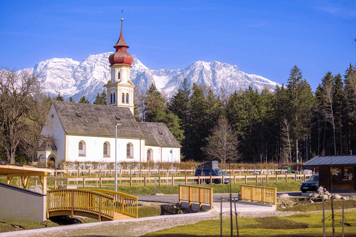 Campingplatz und Kirche vor sommerlicher Bergkulisse
