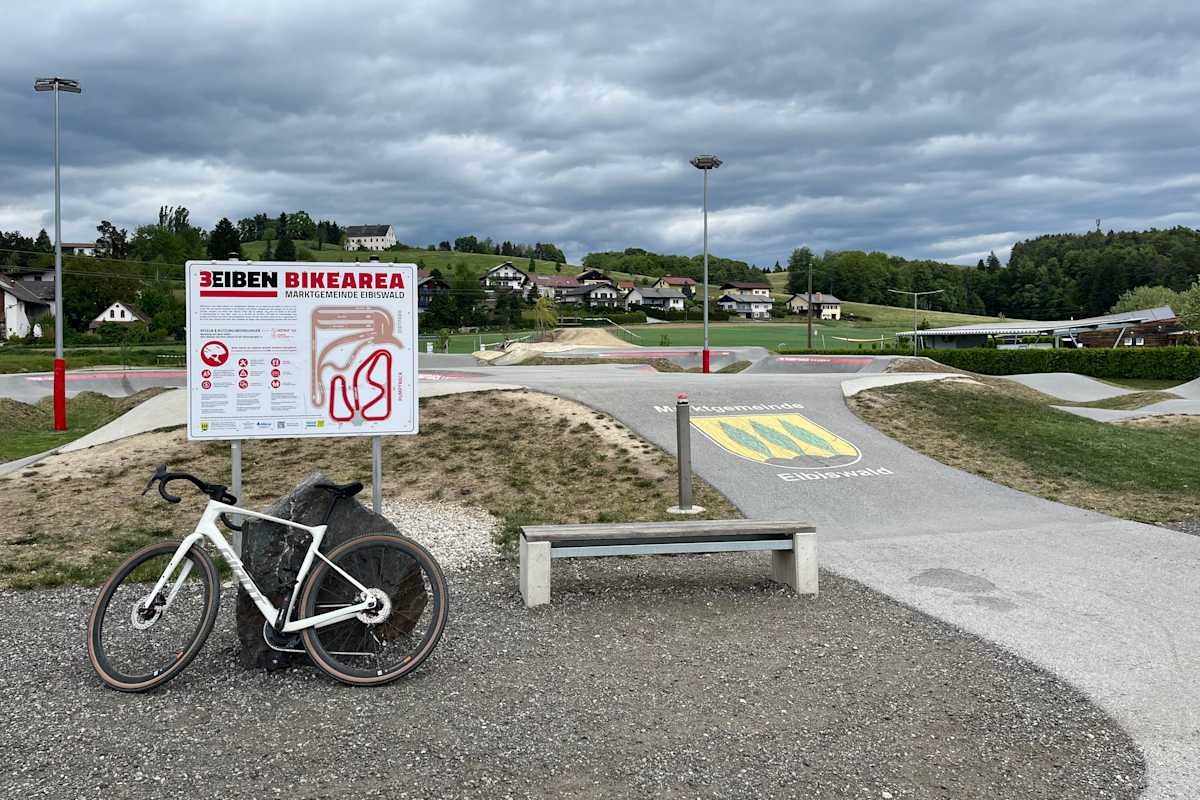 Der „3Eiben Pumptrack“ in Eibiswald: Übersichtstafel und angelehntes Rad vor dem Gelände des Pumptracks
