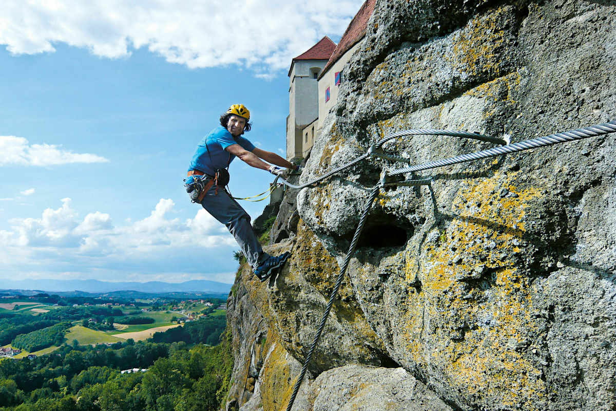 Mann hängt im Riegersburg Klettersteige an einer beinahe vertikalen Felswand